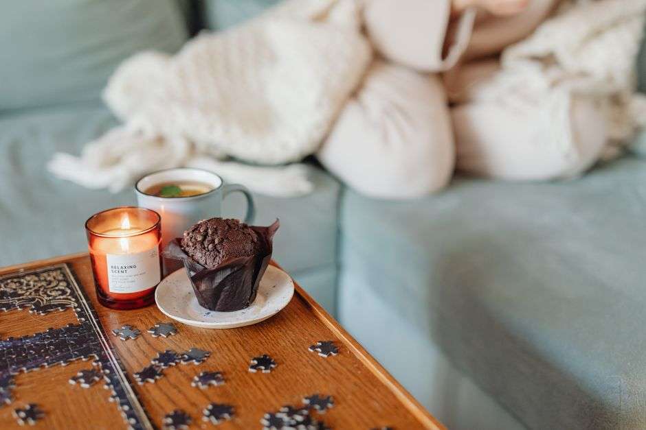 Świeca, muffinka na talerzyku i kawa na stole przy układaniu puzzli.