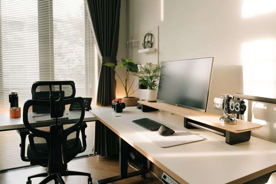 Nowoczesne stanowisko pracy z ergonomicznym fotelem, monitorem na podstawce i roślinami.