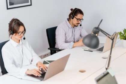 Kobieta i mężczyzna w słuchawkach pracują przy laptopach w biurze.