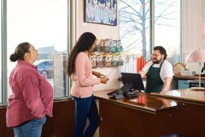 Kobiety przy ladzie zamawiają jedzenie u pracownika restauracji obsługującego kasę.
