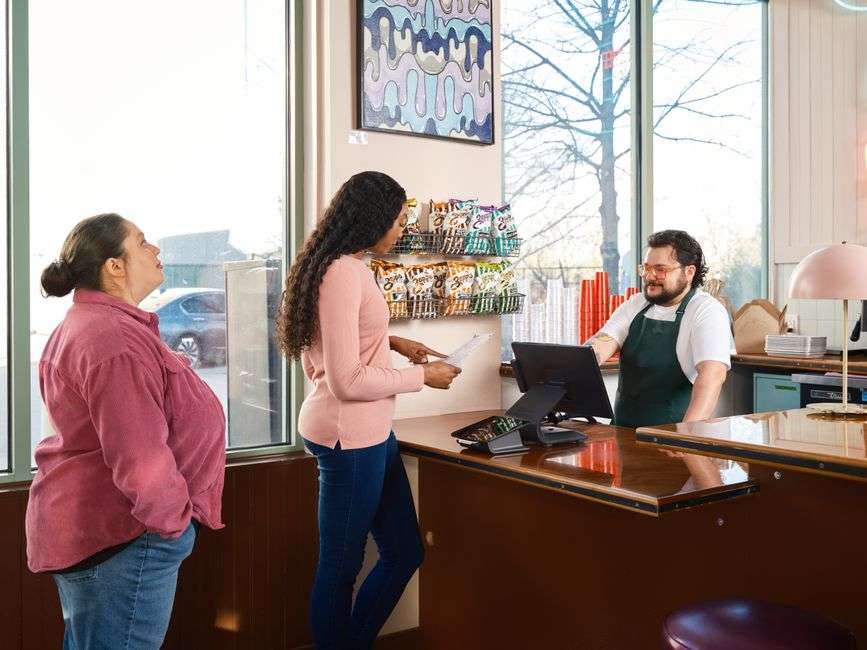 Kobiety przy ladzie zamawiają jedzenie u pracownika restauracji obsługującego kasę.