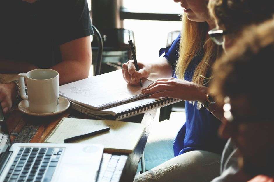 Trzy osoby pracujące wspólnie przy stole z laptopem i notatnikiem.