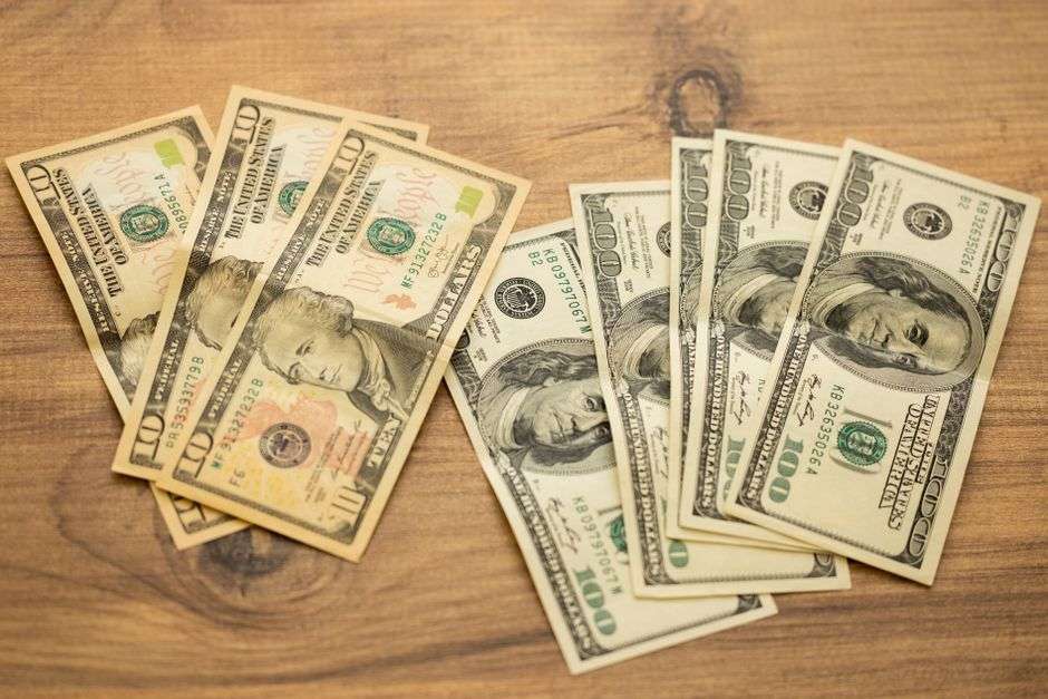 Banknoty dziesięcio- i studolarowe leżące w nieładzie na drewnianym blacie.