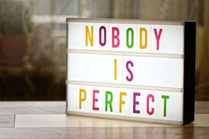 Podświetlana tablica z kolorowym napisem NOBODY IS PERFECT stojąca na stole.