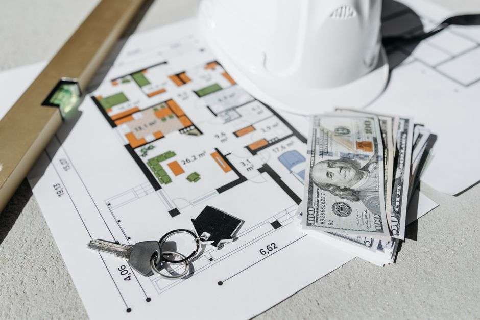 Projekt architektoniczny domu, klucze, pieniądze i poziomica na betonowym podłożu.