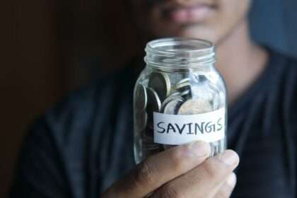 Mężczyzna trzyma szklany słoik wypełniony monetami z naklejką „SAVINGS”.