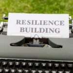 Zabytkowa maszyna do pisania z kartką papieru z napisem "RESILIENCE BUILDING" na trawie.