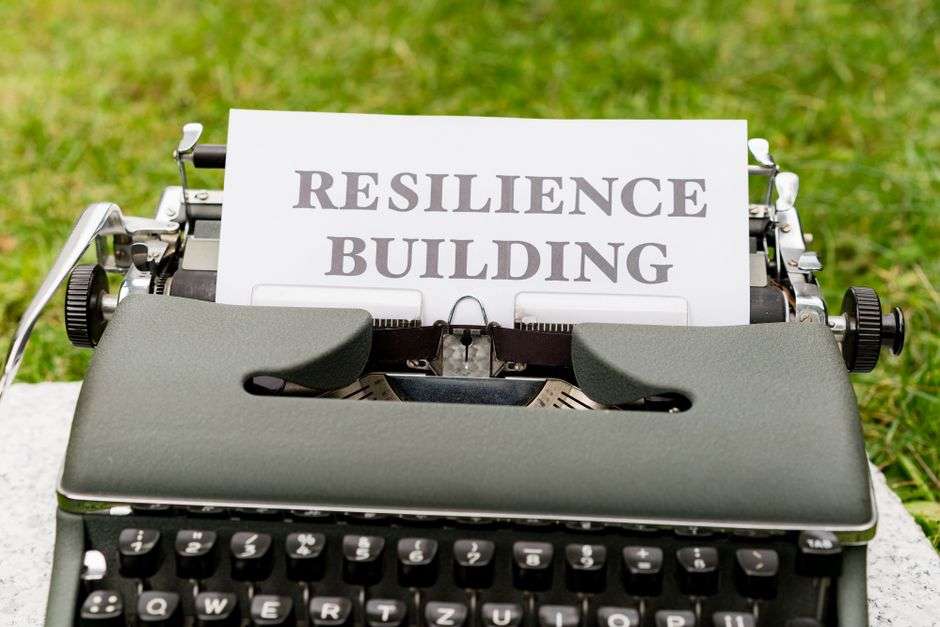 Zabytkowa maszyna do pisania z kartką papieru z napisem "RESILIENCE BUILDING" na trawie.