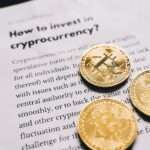 Trzy złote monety z symbolem Bitcoina leżące na kartce z tekstem o kryptowalutach.
