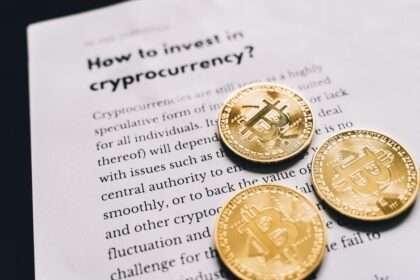 Trzy złote monety z symbolem Bitcoina leżące na kartce z tekstem o kryptowalutach.