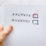 Ręka trzyma kartkę z wyrazami BALANCE i BURNOUT oraz zaznaczonym wyborem BALANCE.