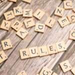 Rozrzucone klocki do gry w Scrabble z ułożonym napisem „RULES” na drewnianym stole.