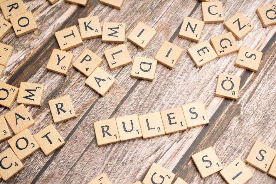 Rozrzucone klocki do gry w Scrabble z ułożonym napisem „RULES” na drewnianym stole.