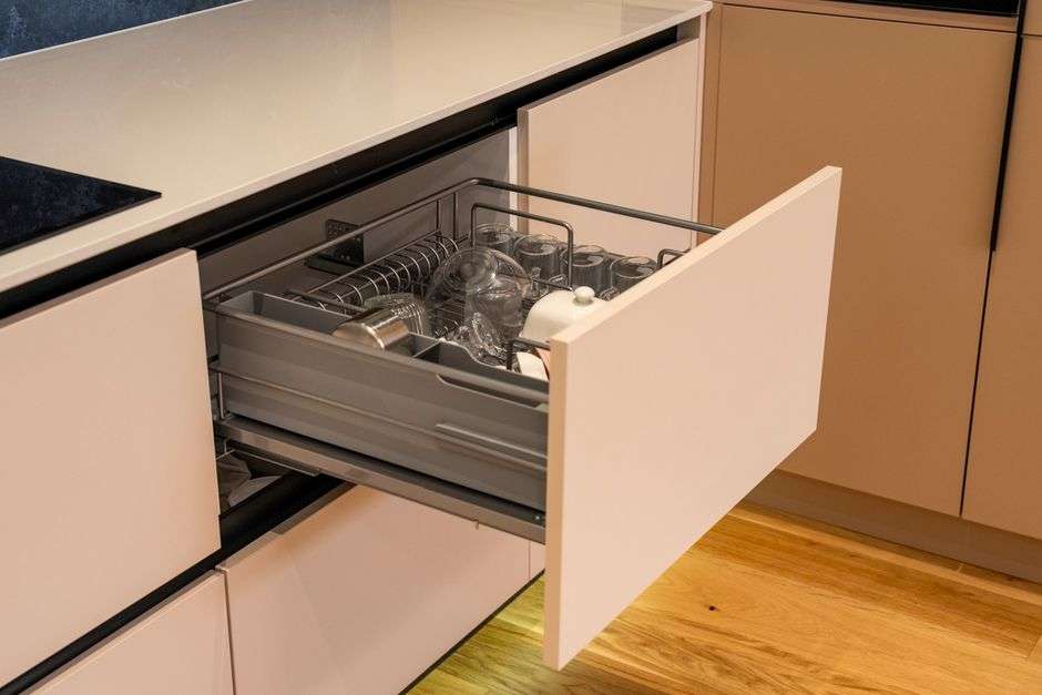 Otwarta szuflada kuchenna z metalowym koszem na naczynia i szklanki.