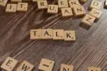 Drewniane płytki z literami ułożone w słowo TALK na ciemnym drewnianym tle.