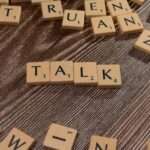 Drewniane płytki z literami ułożone w słowo TALK na ciemnym drewnianym tle.
