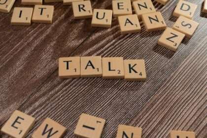 Drewniane płytki z literami ułożone w słowo TALK na ciemnym drewnianym tle.