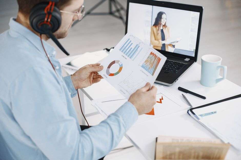 Mężczyzna w słuchawkach pracuje przy laptopie, analizując wykresy na papierowym dokumencie.